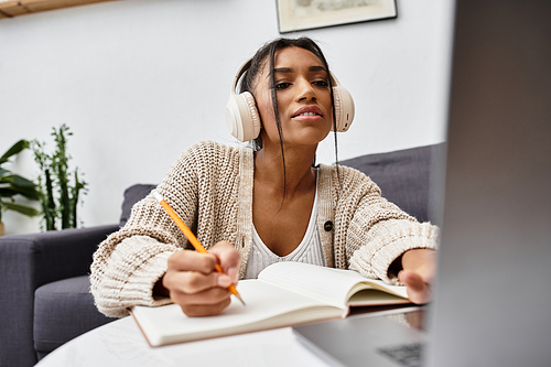 A dedicated young woman focuses on her studies at home while using a laptop and writing notes.