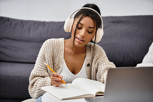 With headphones on, a woman takes notes while studying at her comfortable home desk