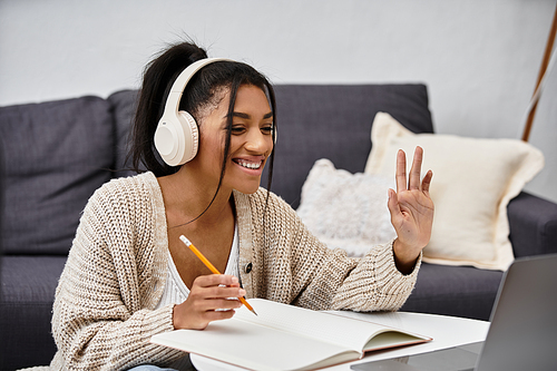 A young woman engages in remote learning from her cozy home setting, smiling and focused.