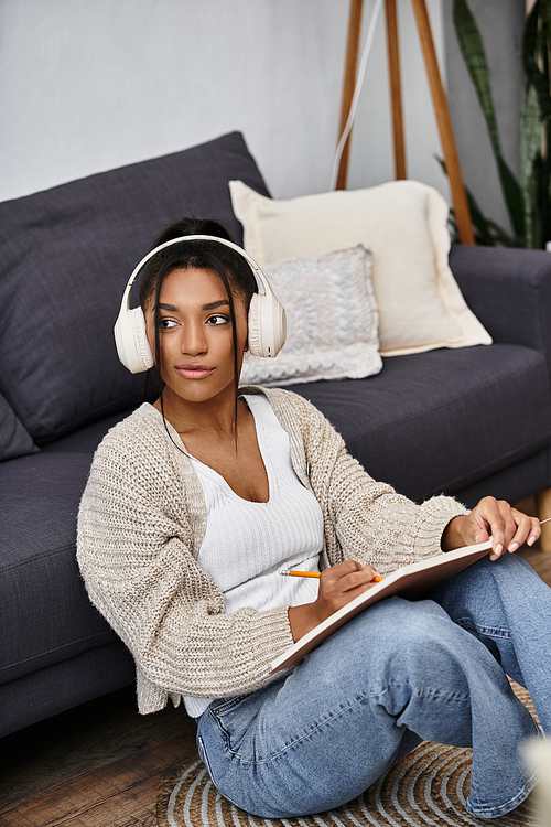 A young woman sits on the floor, taking notes in her notebook, while studying at home.