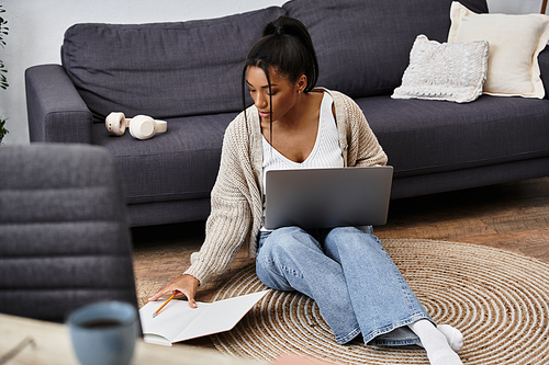 The young woman is deeply focused on her studies while sitting on the floor at home.