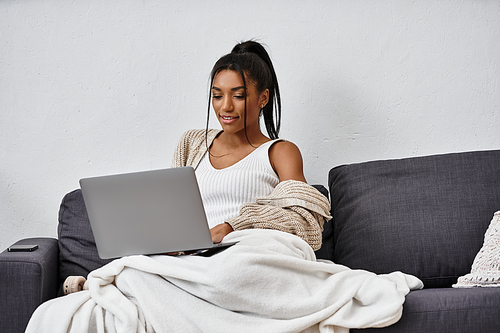 The young woman focuses intently on her laptop while comfortably seated in her living room.