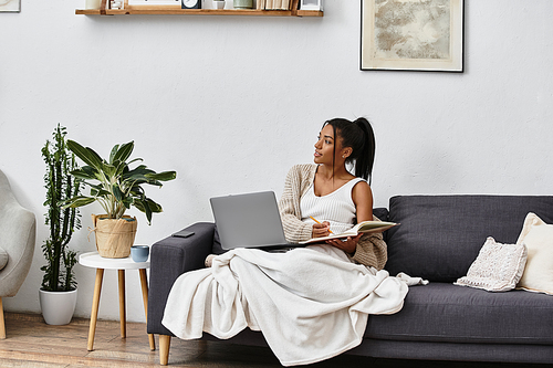 A beautiful young woman is immersed in her studies, seated on a couch at home.