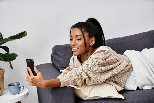 A young woman attentively studies from her home, smiling as she interacts with her smartphone.