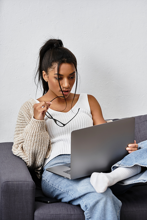 The woman intently focuses on her laptop while relaxing in her stylish living space at home.