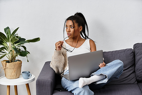 A young woman engages in remote learning at home, thoughtfully studying on her couch.