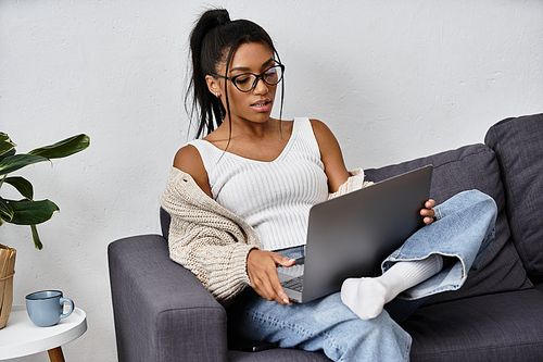 A young woman is focused on her laptop, studying comfortably in a cozy living space.