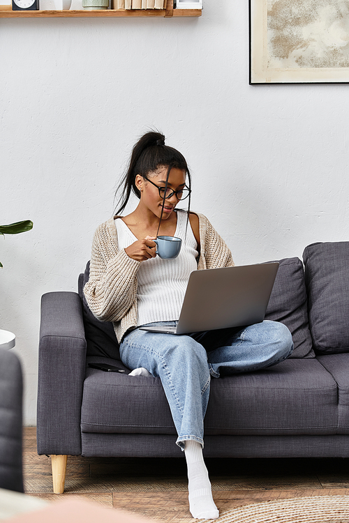 A beautiful young woman studies remotely, sipping coffee on her cozy couch in a peaceful setting.