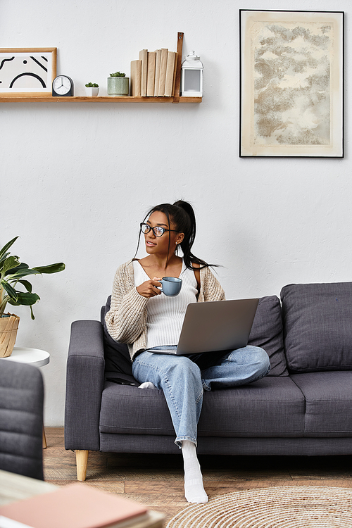 A young woman studies comfortably from her living room, holding a warm cup of coffee and smiling.