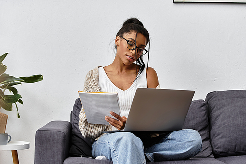 A young woman focused on her remote studies, sitting comfortably on a couch with a laptop.