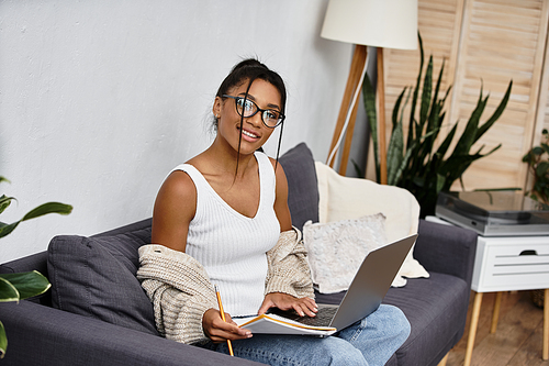 A young woman happily studies from her home, surrounded by greenery and comfort.