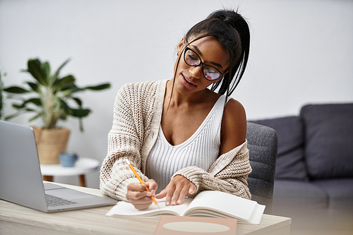 This young woman is engaged in remote study, taking notes in her cozy home setting.