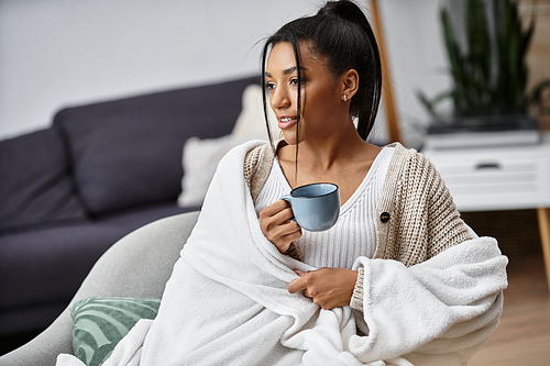 Wrapped in a soft blanket, a young woman studies while savoring her favorite beverage.