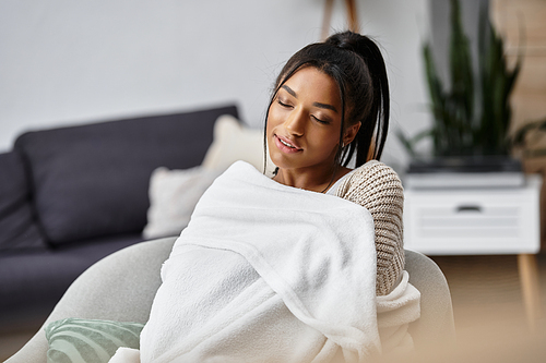 A young woman sits comfortably at home, studying remotely and embracing warmth.