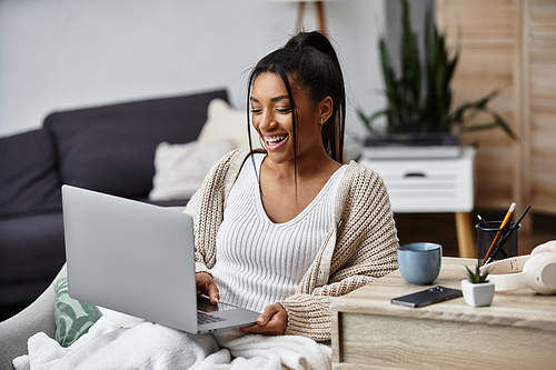 A cheerful young woman engages in remote studying at home while enjoying her cozy environment.