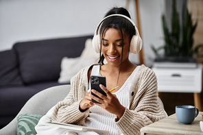 A young woman enjoys studying remotely in a cozy setting, smiling at her phone.