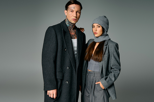 A stylish young couple poses confidently in warm winter attire against a muted background.