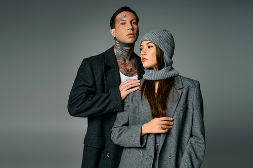 A trendy young couple stands close together, showcasing modern fashion in gray tones.