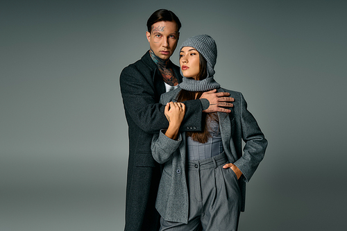 A fashionable young couple showcases modern gray attire and striking poses together.