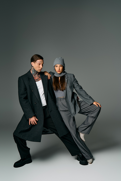 A stylish couple shows off trendy street style with unique poses and outfits in studio light.