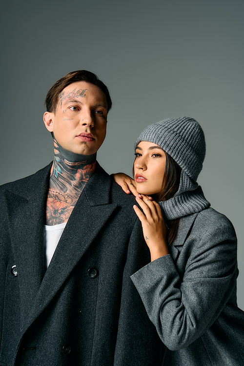 A young couple embraces, showcasing their fashionable attire and tattoos in a chic location.