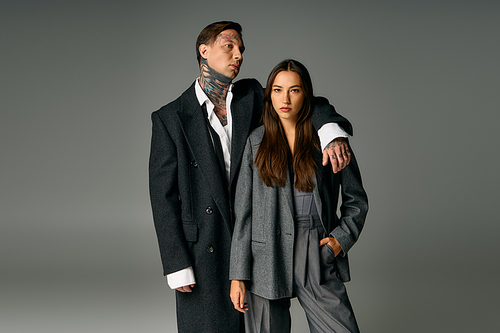 A fashionable young couple displays confidence in elegant gray attire, showcasing modern style.