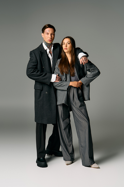 A young attractive couple stands close together in fashionable gray attire, exuding confidence.