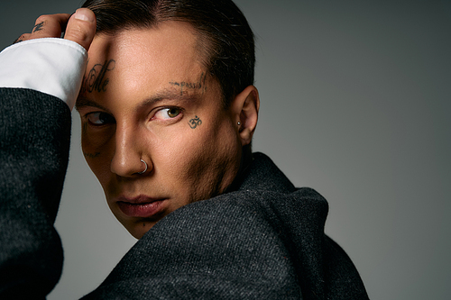 A young man showcases unique tattoos while staring with an enigmatic expression.