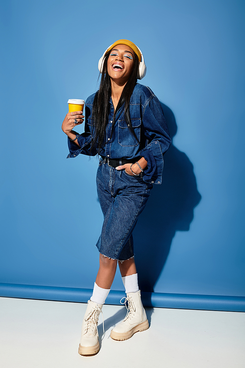 A joyful young woman in trendy autumn attire holds a warm drink, radiating happiness.