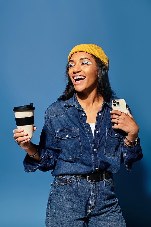 A vibrant young woman smiles with a coffee cup and smartphone, dressed in cozy autumn fashion.