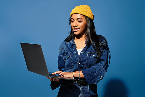 A young woman comfortably engages with her laptop, dressed for warm autumn days in vibrant attire.