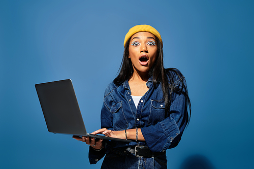 A young woman in a stylish autumn ensemble expresses surprise while using her laptop.