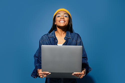 A young woman dressed warmly in autumn clothing beams joyfully while showcasing her laptop.