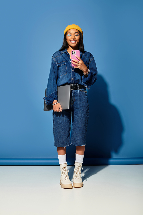 A young woman with a warm smile showcases her trendy autumn outfit while holding a phone.