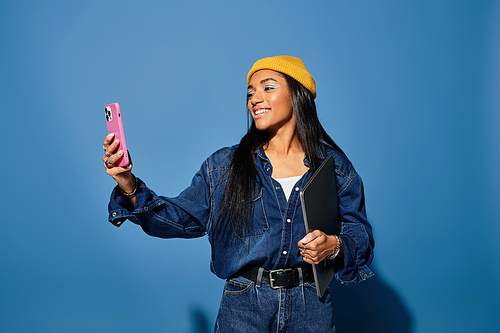 A young woman dressed in warm autumn clothing happily captures a selfie while posing.