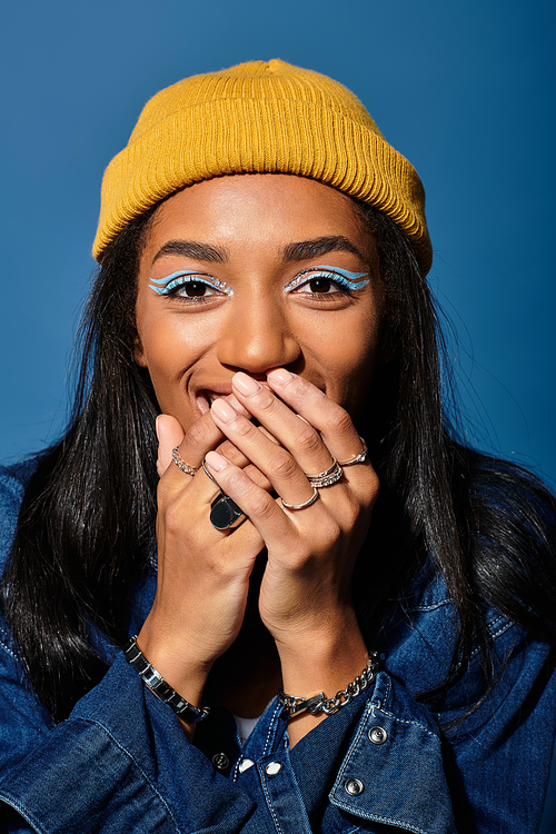 A young woman in a cozy autumn outfit joyfully covers her smile with her hands.