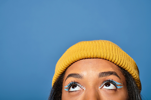 A young woman in a cozy yellow beanie admires the sky, showcasing her unique eye makeup.