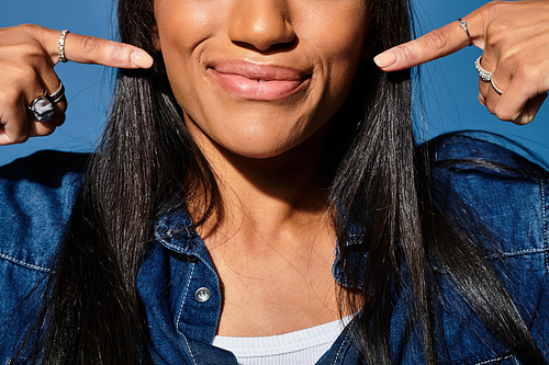 A young woman smiles joyfully, playfully pointing to her lips in autumn fashion.