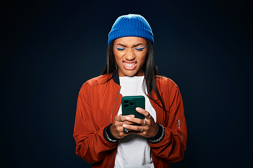 The young woman dressed warmly frowns at her phone, capturing a moment of annoyance or surprise.