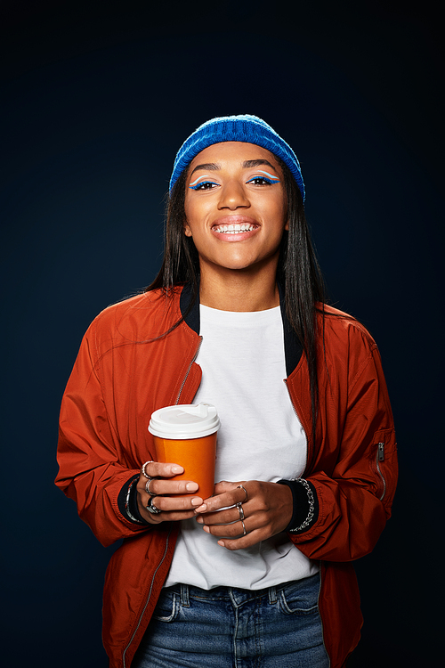 A joyful young woman warms herself with a cup of coffee while dressed in autumn fashion.