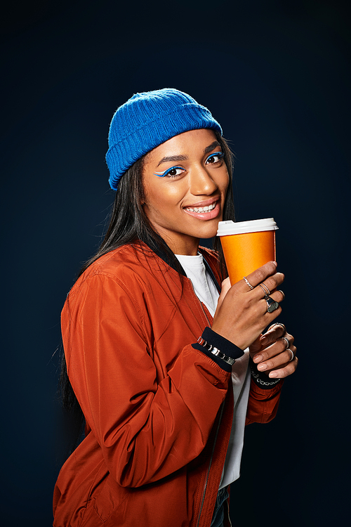 A stylish young woman holds a warm beverage, radiating autumn vibes and joy.