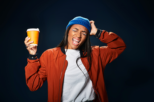 A young woman in cozy autumn gear happily holds a warm drink, celebrating the season.