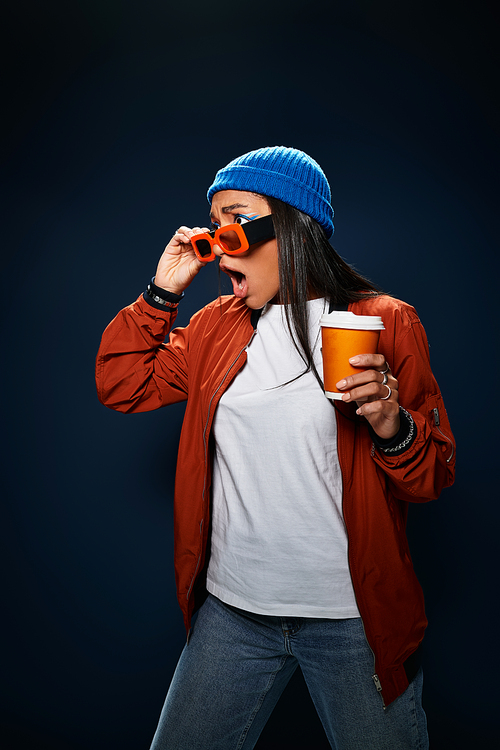 Dressed in fashionable autumn layers, a young woman strikes a fun pose holding a cup.