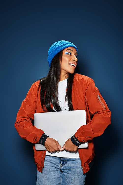 A young woman in trendy autumn clothing joyfully embraces her laptop, exuding charm and warmth.