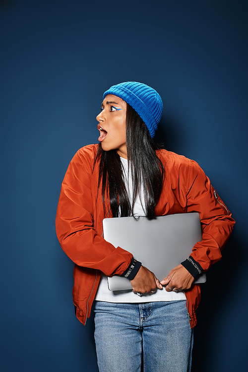 A young woman wearing cozy fall clothing looks surprised while clutching a laptop.