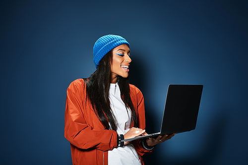 Wearing a trendy outfit, a young woman smiles while using her laptop, embracing autumn style.