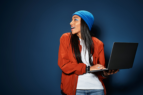 A young woman wearing a vibrant blue beanie and trendy autumn jacket enjoys her laptop.