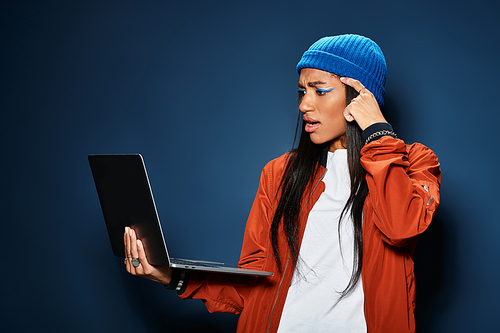 A young woman in warm fall clothing deeply engages with her laptop, expressing curiosity.