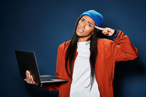 A young woman in a cozy outfit playfully engages with her laptop, showcasing her creativity.