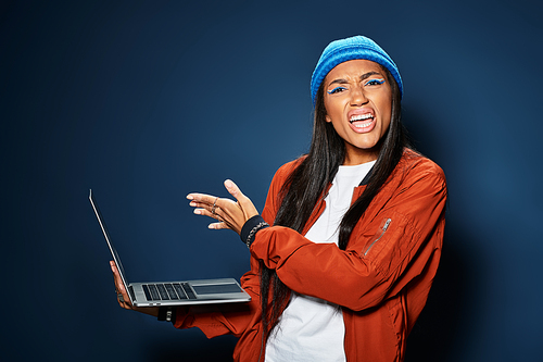 A stylish young woman in autumn clothing shows enthusiasm while engaging with her laptop.